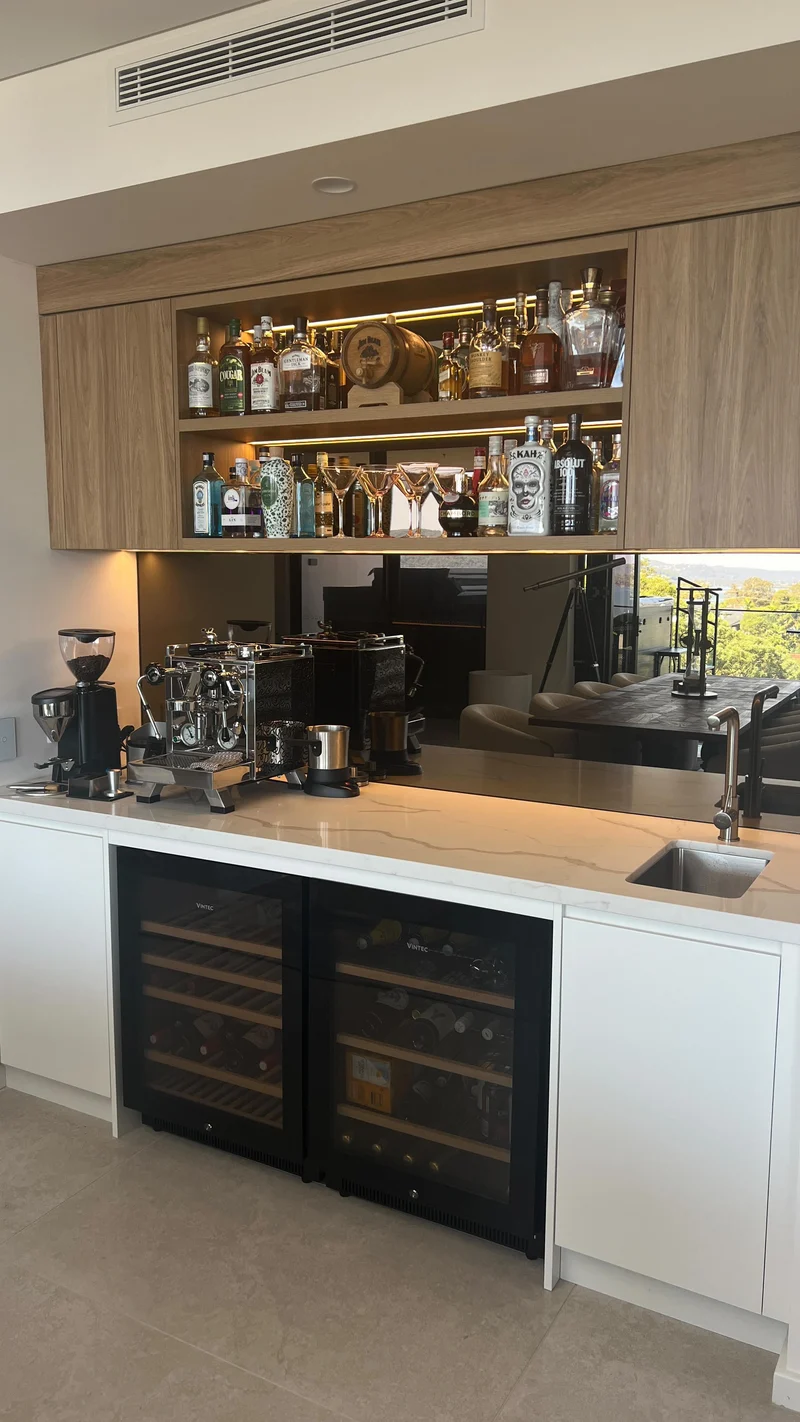 Bronze mirror splashback behind a coffee machine and sink in a home bar with timber cabinetry