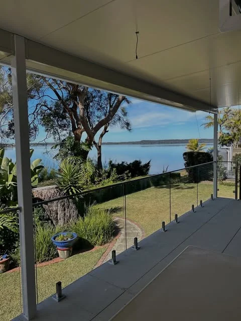 Glass balustrade with stainless steel spigots along a covered veranda overlooking a lake