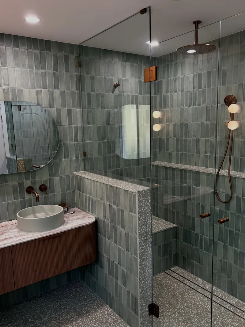 Frameless shower screen with brass fittings in a green tiled bathroom